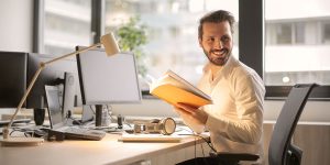smiling man sitting at desk with book in hand